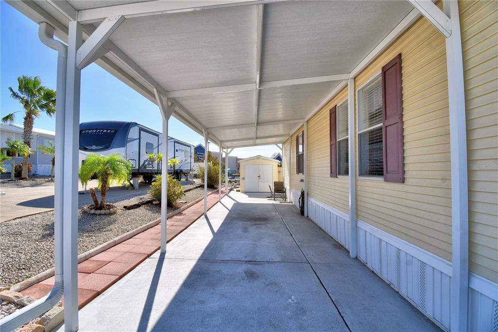 A covered concrete carport runs alongside a yellow mobile home with a detached storage shed — 251 PATTERSON ROAD UNIT I17, HAINES CITY, FL