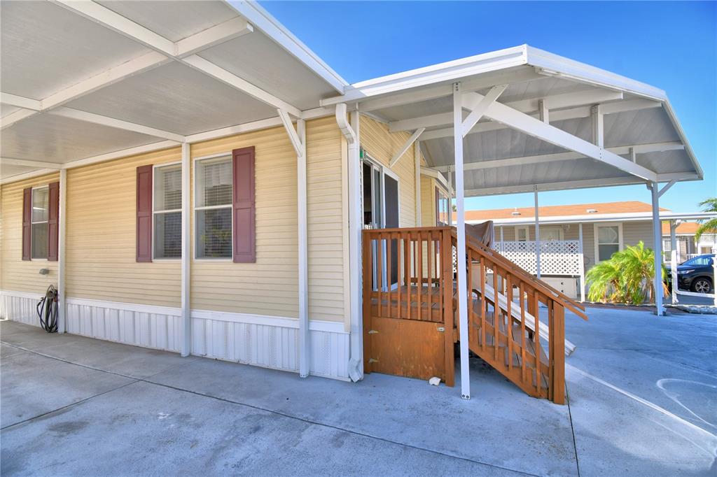 A yellow mobile home exterior with a wooden deck, carport, and concrete driveway — 251 PATTERSON ROAD UNIT I17, HAINES CITY, FL