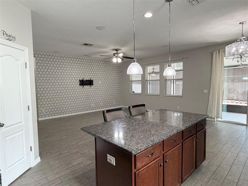 A kitchen island with granite countertops sits in front of a living area with patterned wallpaper — 3272 MANGROVE ISLAND DRIVE, ORLANDO, FL