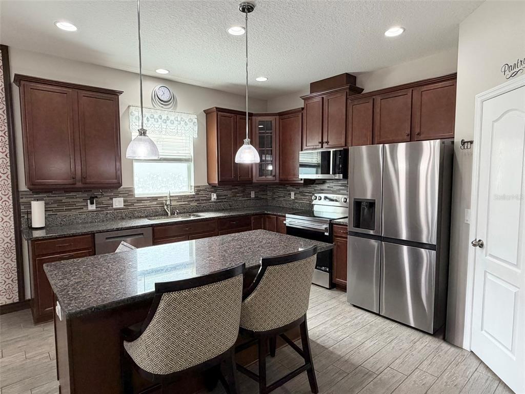 A kitchen features dark wood cabinets, granite countertops, a center island, and stainless steel appliances — 3272 MANGROVE ISLAND DRIVE, ORLANDO, FL