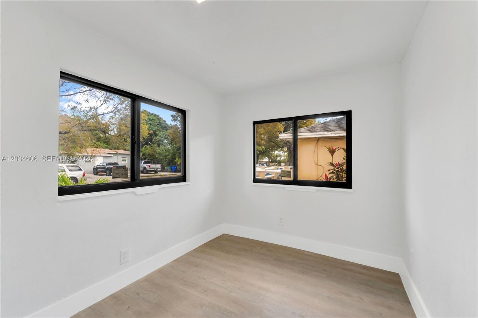 A bright, empty room features white walls, light wood-look flooring, and two black-framed windows — 2428 NW 28th St, Miami FL 33142, MIAMI, FL
