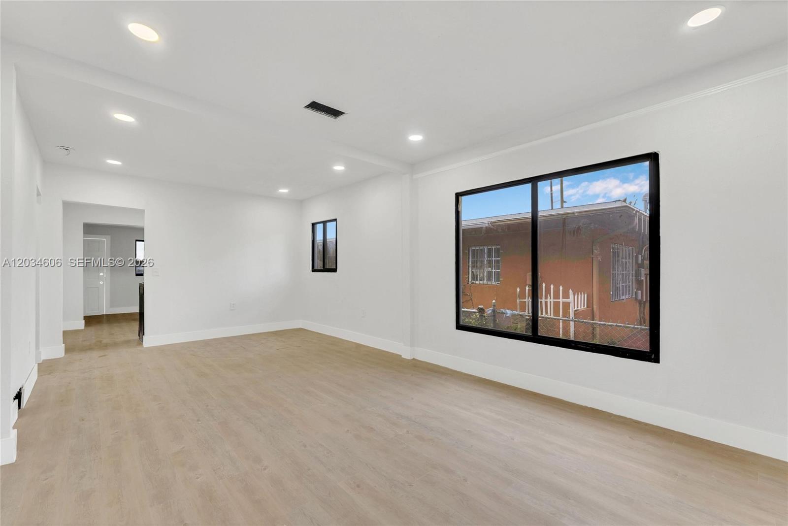 An empty room features light wood-look flooring, white walls, recessed lighting, and two windows — 2428 NW 28th St, Miami FL 33142, MIAMI, FL