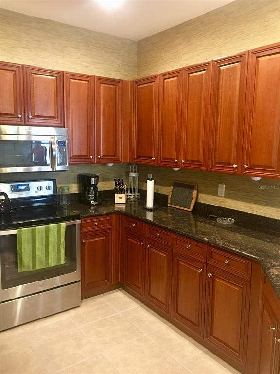 A kitchen features cherry wood cabinets, dark granite countertops, and stainless steel appliances — 17084 ACAPULCO ROAD UNIT 223, PUNTA GORDA, FL
