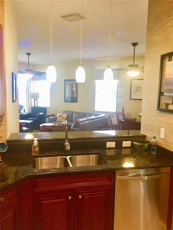 A kitchen sink and stainless steel dishwasher are in the foreground with a living area beyond — 17084 ACAPULCO ROAD UNIT 223, PUNTA GORDA, FL