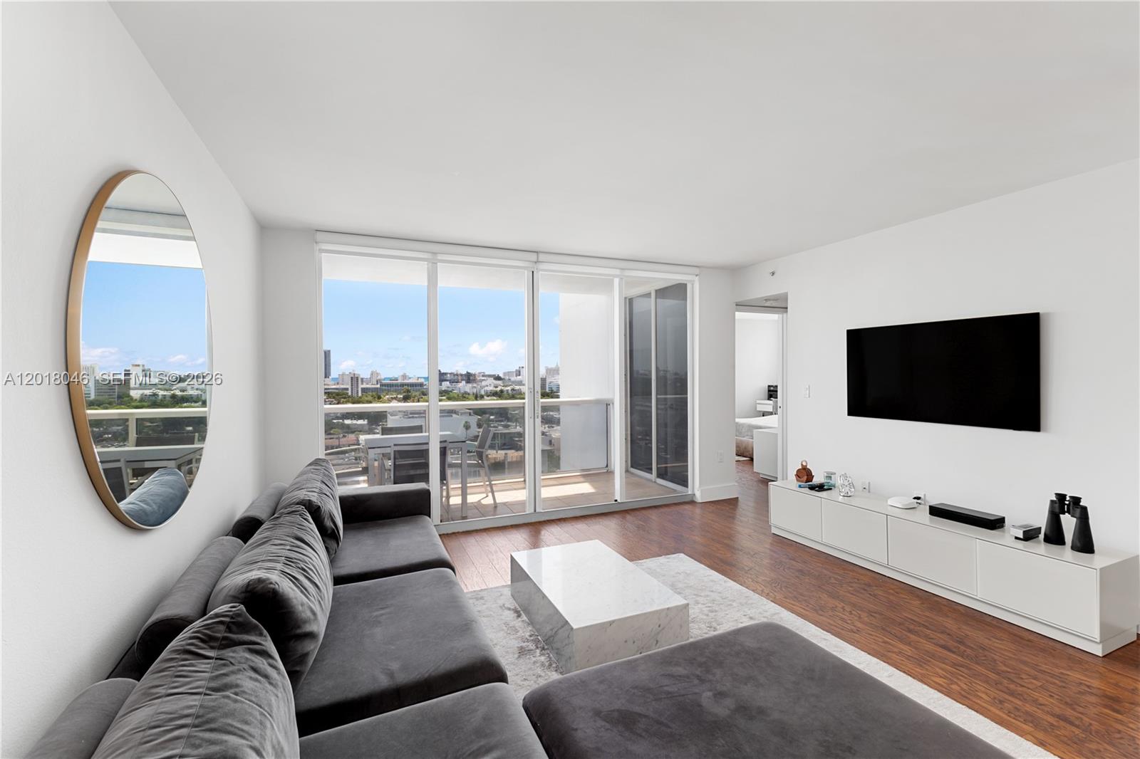 A living room features a gray sectional, marble coffee table, wall-mounted television, and balcony access — 1800 Sunset Harbour Dr # 1601, Miami Beach FL 33139, MIAMI BEACH, FL