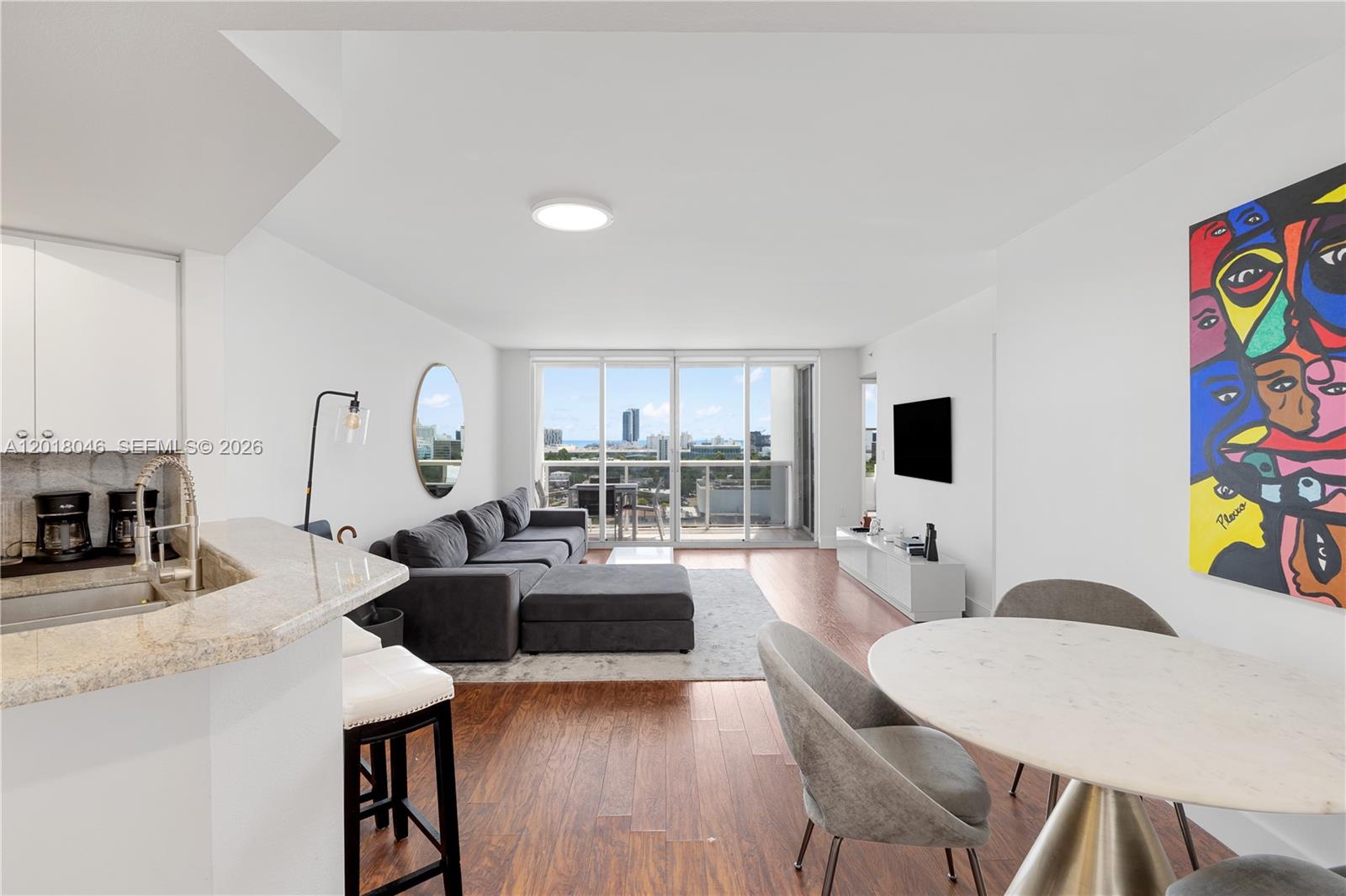 A modern living and dining area features hardwood floors, a gray sectional, and balcony views — 1800 Sunset Harbour Dr # 1601, Miami Beach FL 33139, MIAMI BEACH, FL