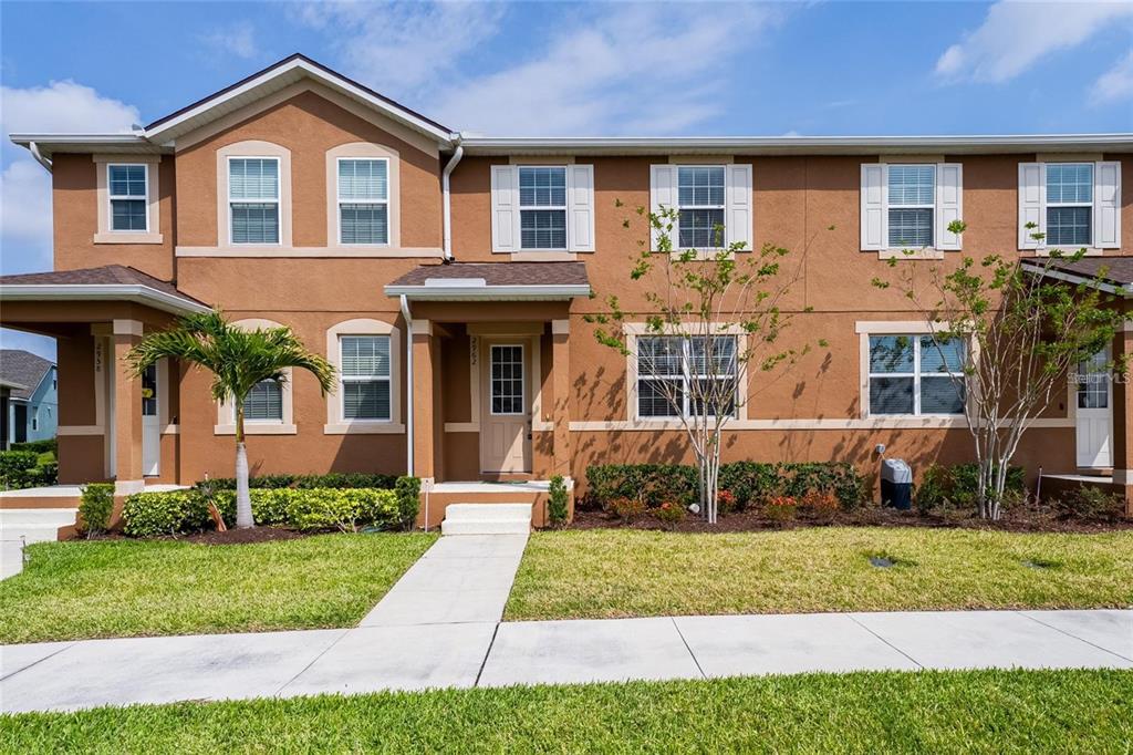 A two-story tan townhouse with white trim, a front porch, and a small front lawn — 2962 FIREBUSH WAY, CLERMONT, FL