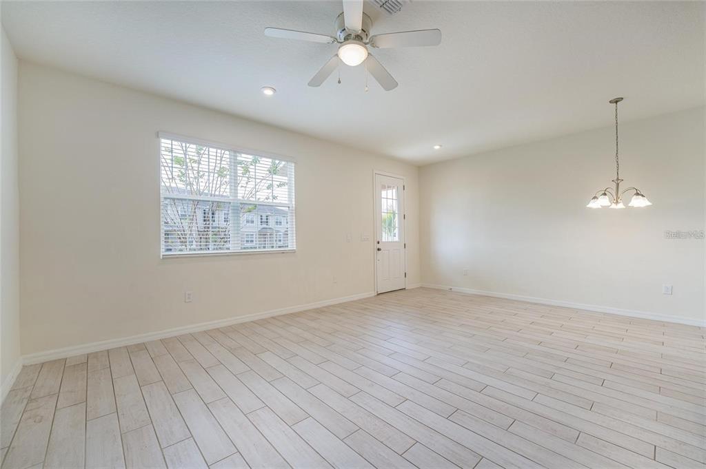 A bright, empty room features light-colored wood-look tile flooring, a ceiling fan, and a chandelier — 2962 FIREBUSH WAY, CLERMONT, FL