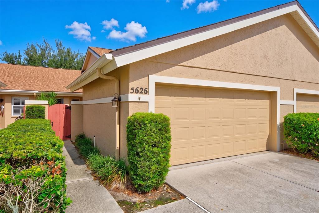 A beige house exterior features a single-car garage, a concrete driveway, and manicured green hedges — 5626 MONTE ROSSO ROAD, SARASOTA, FL