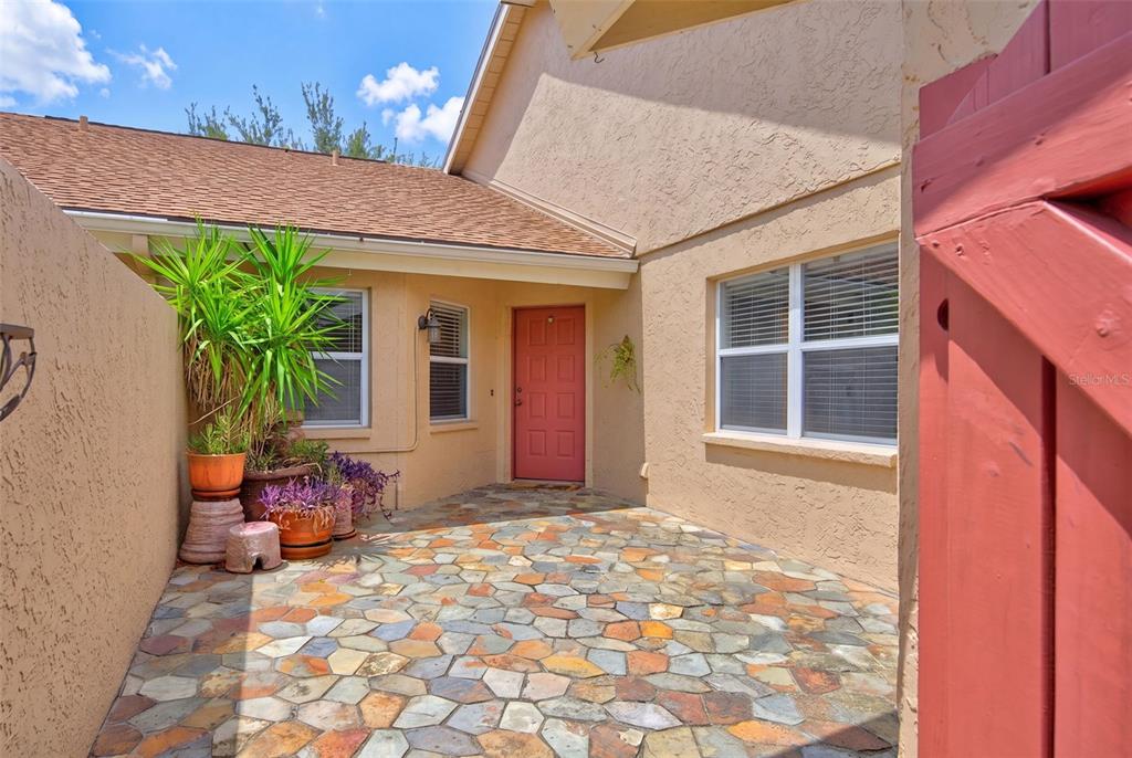 A stone-paved courtyard leads to a red front door of a tan stucco house — 5626 MONTE ROSSO ROAD, SARASOTA, FL