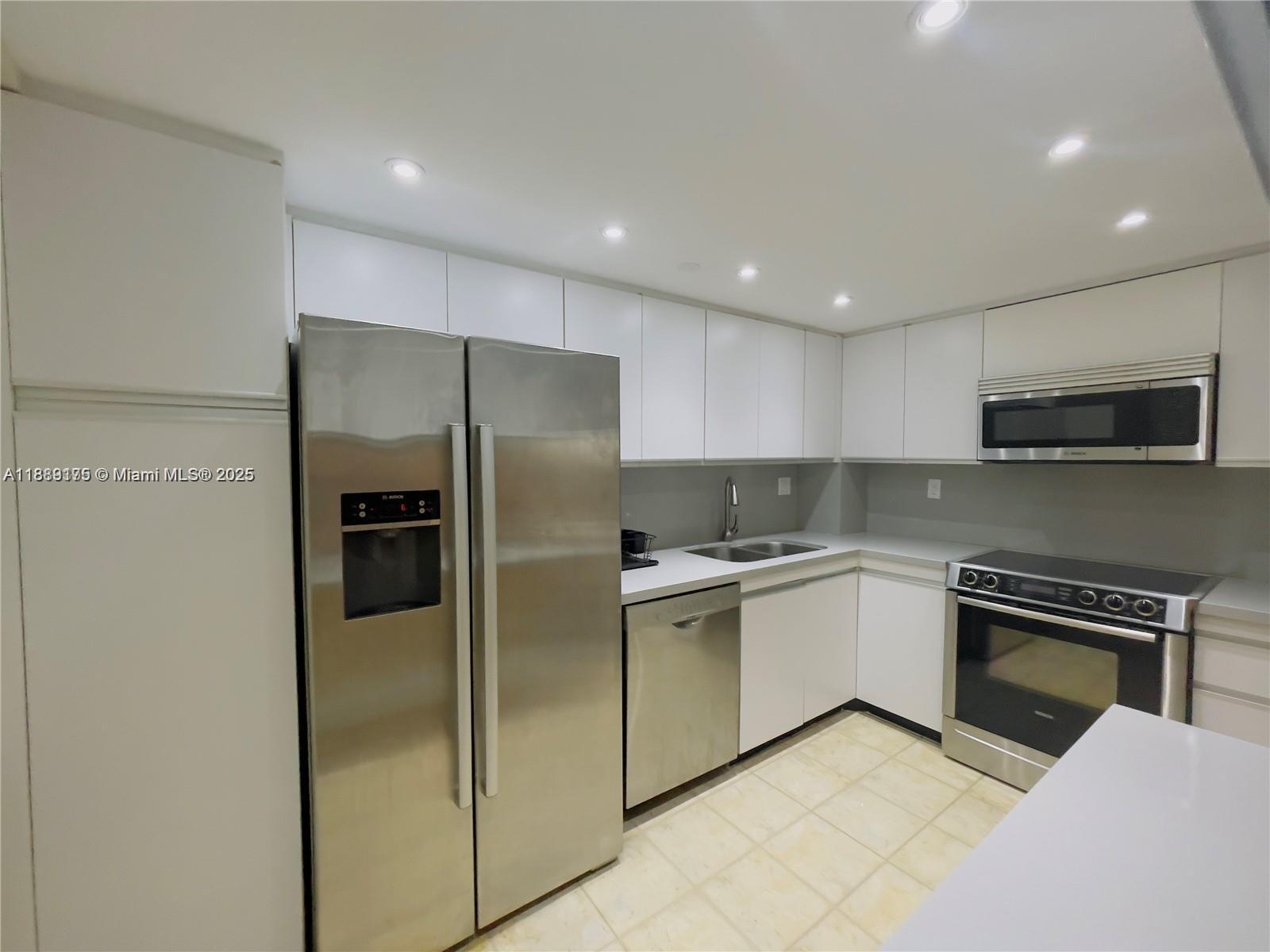 A kitchen features white cabinetry, stainless steel appliances, and light-colored tile flooring — 2000 Towerside # 309, Miami FL 33138, MIAMI, FL