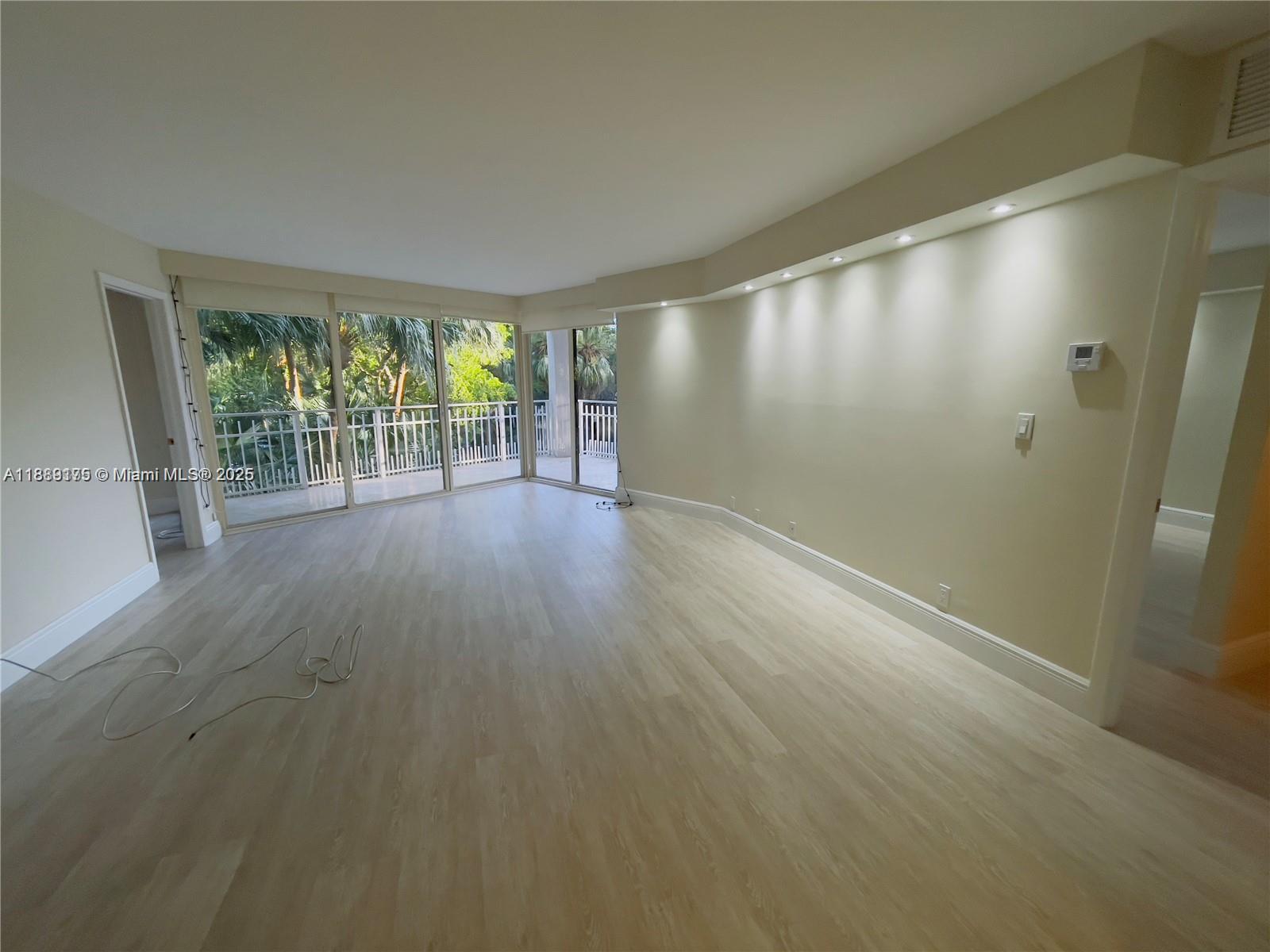 An empty living room features light wood-look flooring, recessed lighting, and a balcony with greenery — 2000 Towerside # 309, Miami FL 33138, MIAMI, FL