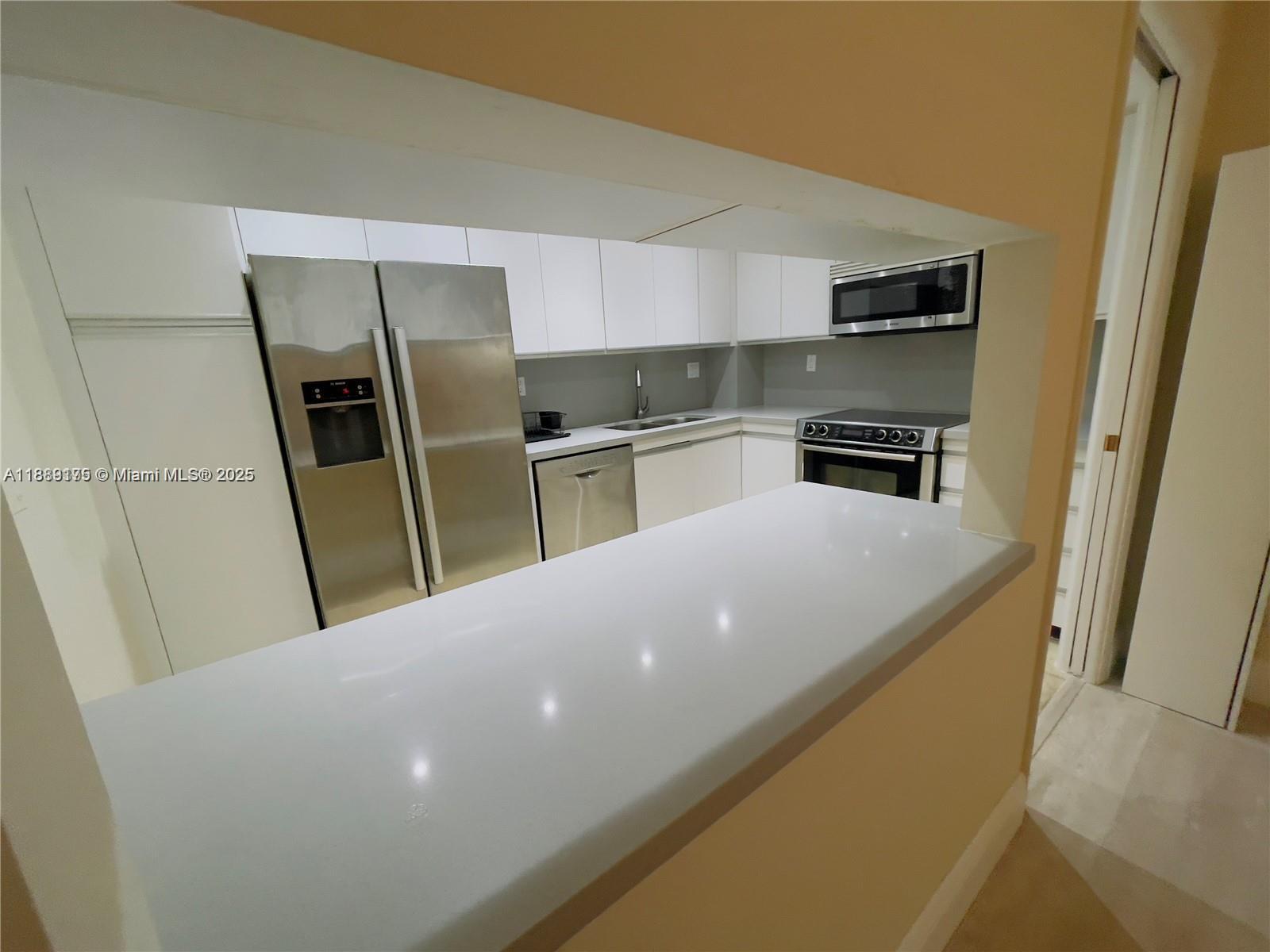 A kitchen features white cabinets, stainless steel appliances, and a white countertop breakfast bar — 2000 Towerside # 309, Miami FL 33138, MIAMI, FL