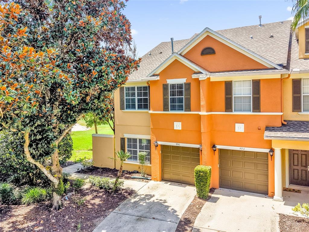 An exterior view of two attached townhomes with orange stucco walls and brown garage doors — 906 ASSEMBLY COURT, KISSIMMEE, FL