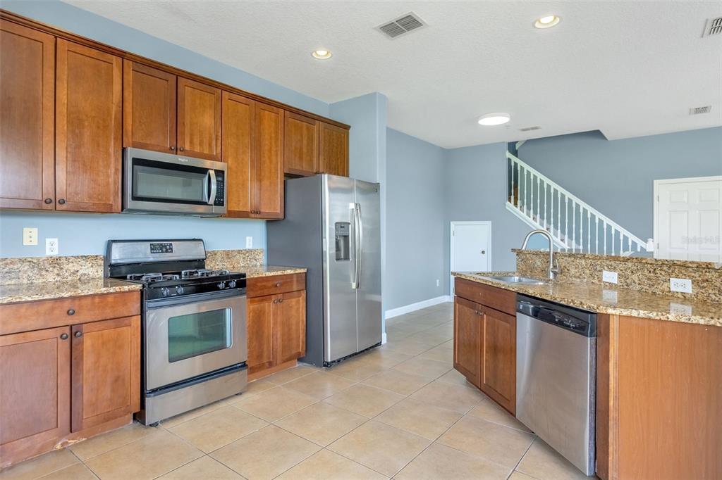 A kitchen with wood cabinets, granite countertops, stainless steel appliances, and a staircase in back — 906 ASSEMBLY COURT, KISSIMMEE, FL