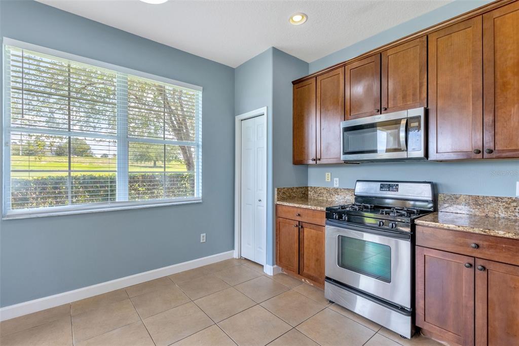 A kitchen features blue walls, wood cabinets, granite countertops, and a stainless steel stove — 906 ASSEMBLY COURT, KISSIMMEE, FL