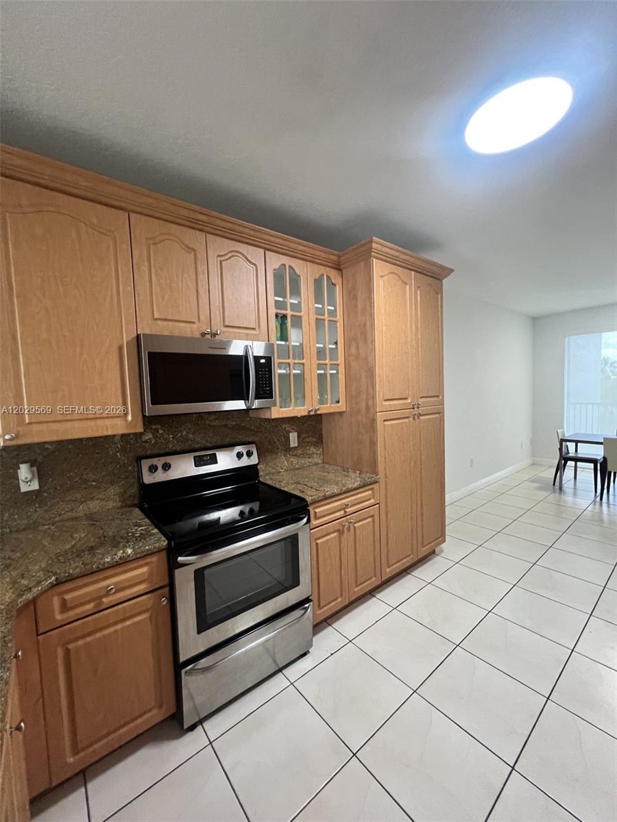 A kitchen features light wood cabinets, granite countertops, stainless steel appliances, and tiled flooring — 10750 NW 66th St # 401, Doral FL 33178, DORAL, FL