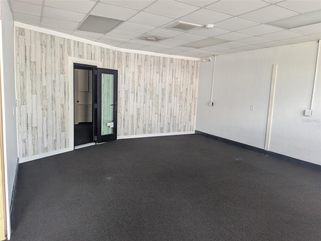 An empty office room features wood-look accent wallpaper, dark carpeting, and a drop ceiling — 5630 PARK BOULEVARD N UNIT A & B, PINELLAS PARK, FL