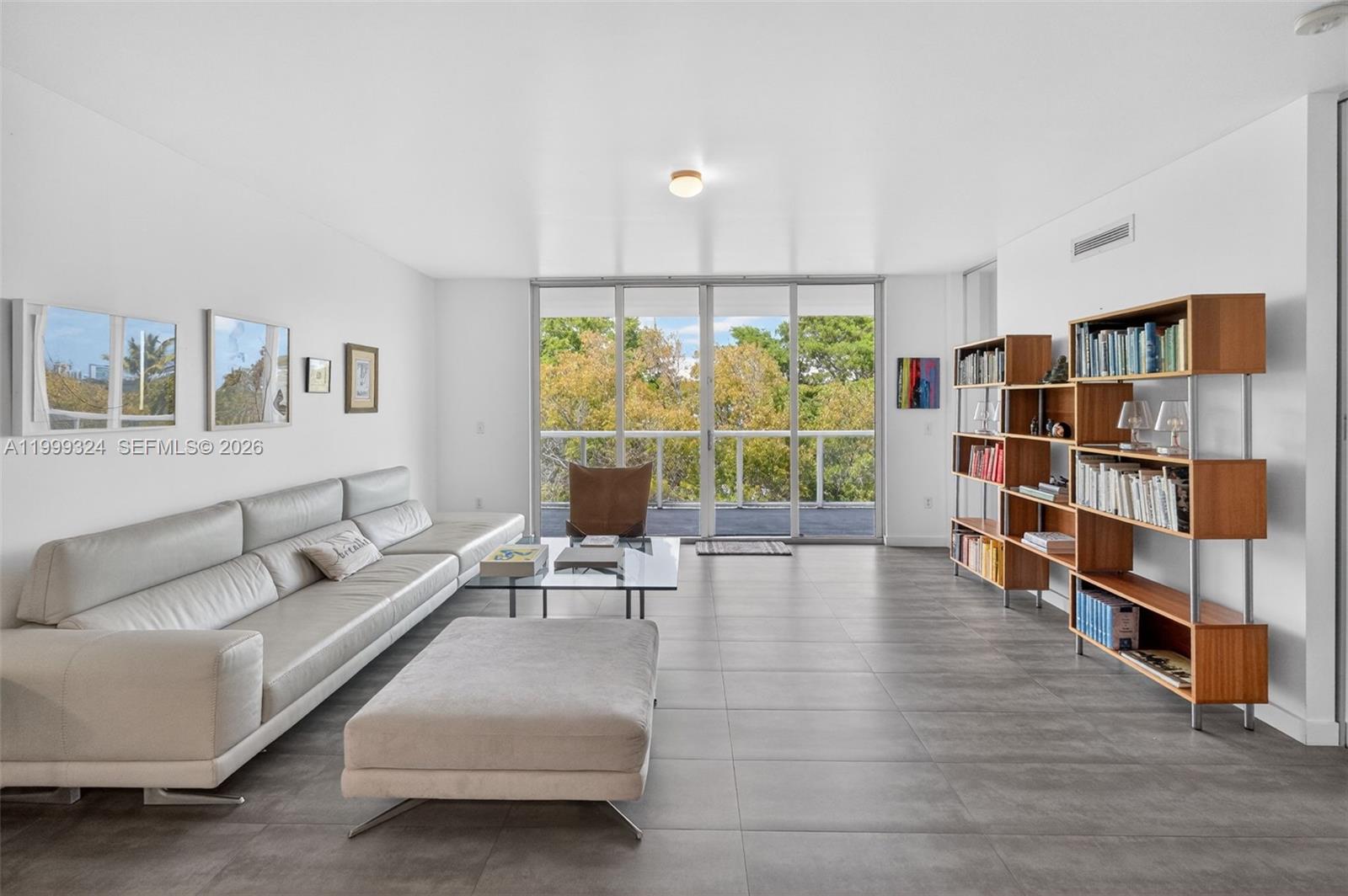 A modern living room features a grey sofa, glass coffee table, and open wooden shelving — 720 NE 62nd St # 404, Miami FL 33138, MIAMI, FL