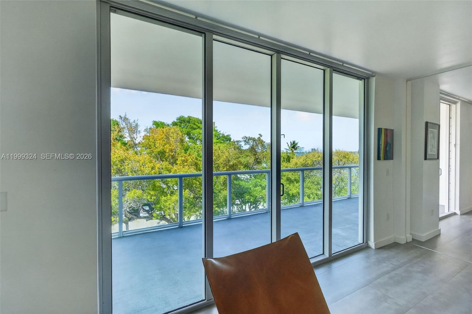 A room with large sliding glass doors opening onto a balcony overlooking lush green trees — 720 NE 62nd St # 404, Miami FL 33138, MIAMI, FL