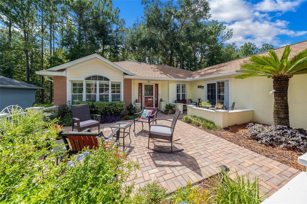 A brick patio with outdoor furniture sits in front of a yellow house with trees — 7240 SW 115TH PLACE, OCALA, FL