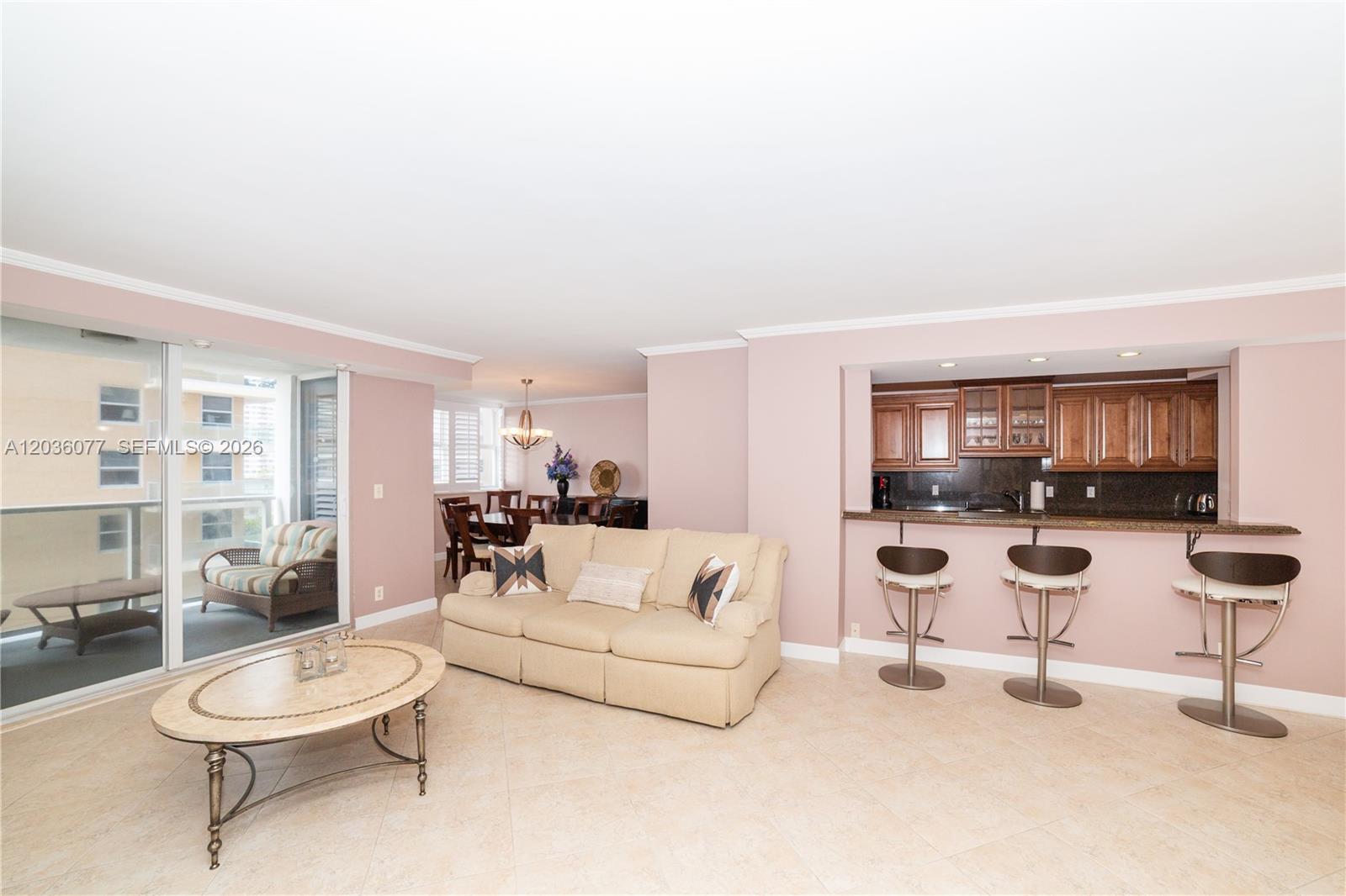 A living room with a beige sofa, breakfast bar, and an adjacent balcony — 1904 S Ocean Dr # 604, Hallandale Beach FL 33009, HALLANDALE BEACH, FL