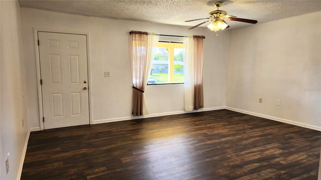 A living room features dark wood-look flooring, a ceiling fan, and a window with curtains — 10405 SW 99TH AVENUE, OCALA, FL