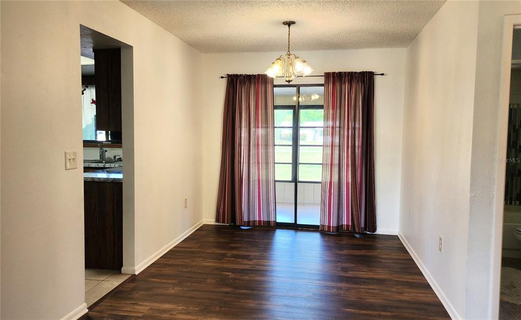 A dining room features dark wood-look flooring, a chandelier, and sliding glass doors with curtains — 10405 SW 99TH AVENUE, OCALA, FL