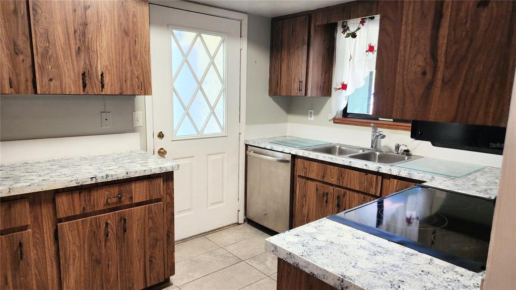 A kitchen features wood-grain cabinets, speckled laminate countertops, a stainless steel dishwasher, and tile flooring — 10405 SW 99TH AVENUE, OCALA, FL