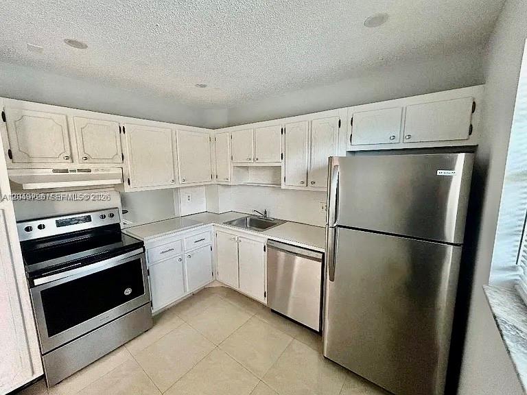 A kitchen features white cabinets, stainless steel appliances, and light-colored tile flooring — 100 Berkley Rd # 210, Hollywood FL 33024, HOLLYWOOD, FL