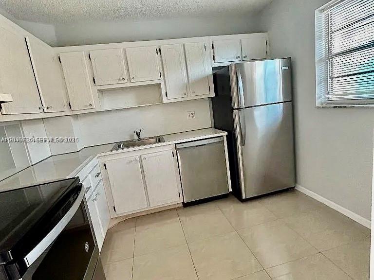 A kitchen features white cabinets, stainless steel appliances, and light-colored tile flooring — 100 Berkley Rd # 210, Hollywood FL 33024, HOLLYWOOD, FL