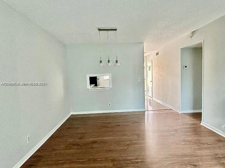 An empty room features light gray walls, wood-look flooring, and a three-light pendant fixture — 100 Berkley Rd # 210, Hollywood FL 33024, HOLLYWOOD, FL