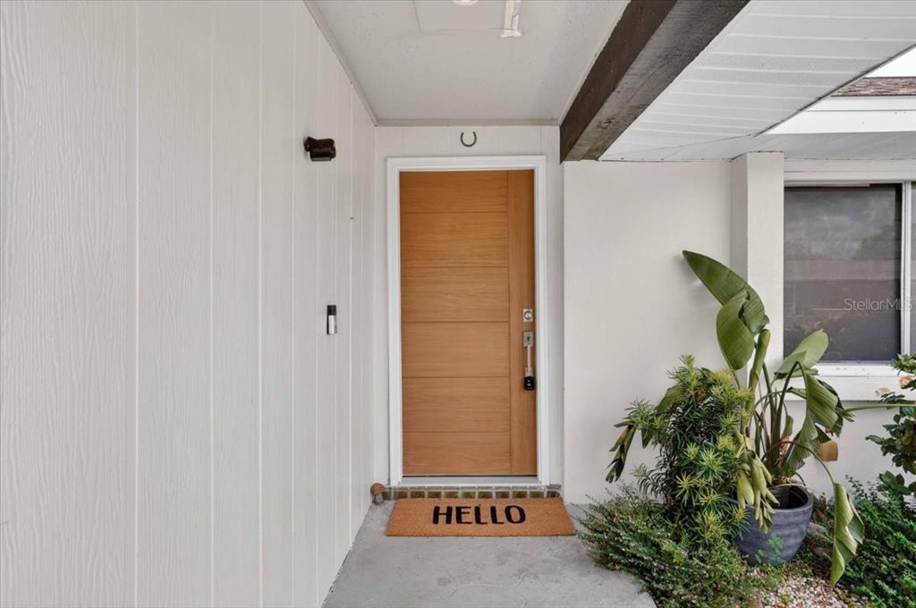 A wooden front door with a "HELLO" mat sits under a covered entryway — 885 FAIRFAX TERRACE NW, PORT CHARLOTTE, FL