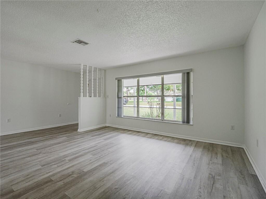 An empty living room features light gray wood-look flooring, white walls, and a large window — 136 16th Avenue, Vero Beach FL 32962, VERO BEACH, FL