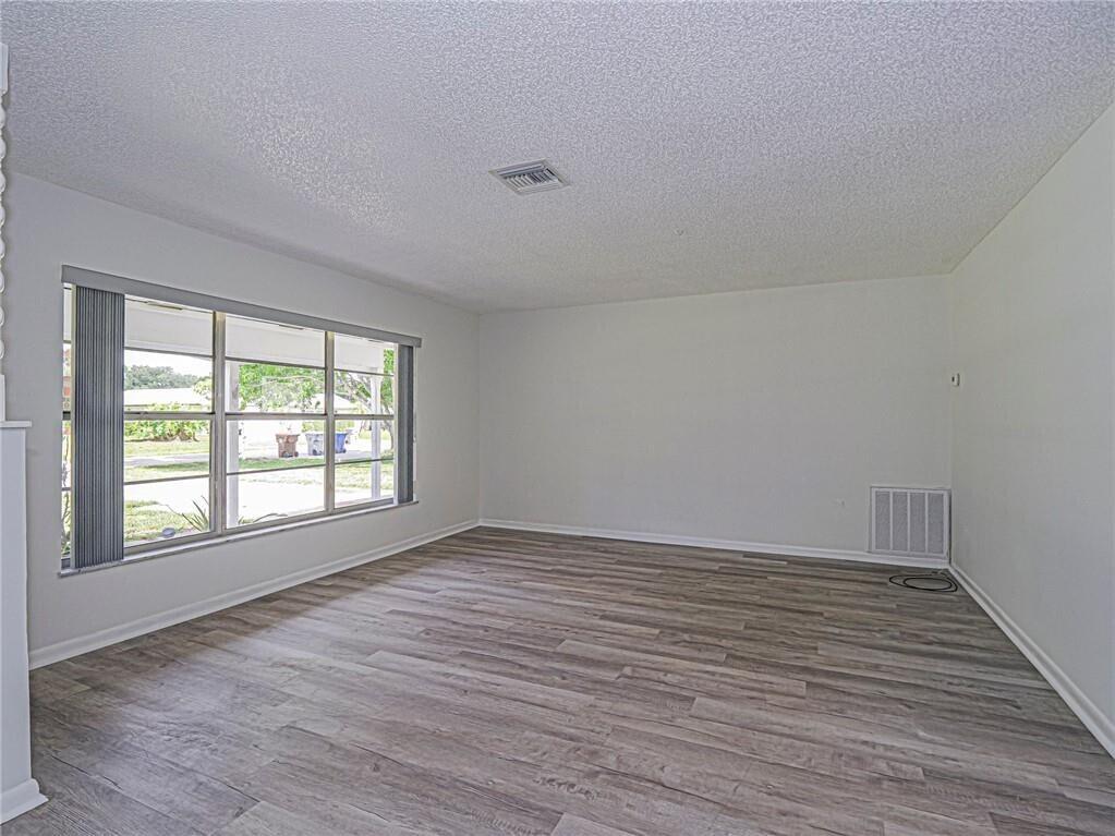 An empty living room features light wood-look flooring, white walls, and a large window — 136 16th Avenue, Vero Beach FL 32962, VERO BEACH, FL