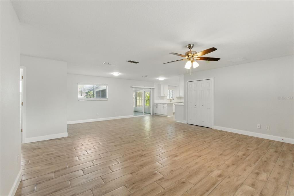 A spacious living room features light wood-look tile flooring, white walls, and a ceiling fan — 8255 PAMLICO STREET, ORLANDO, FL