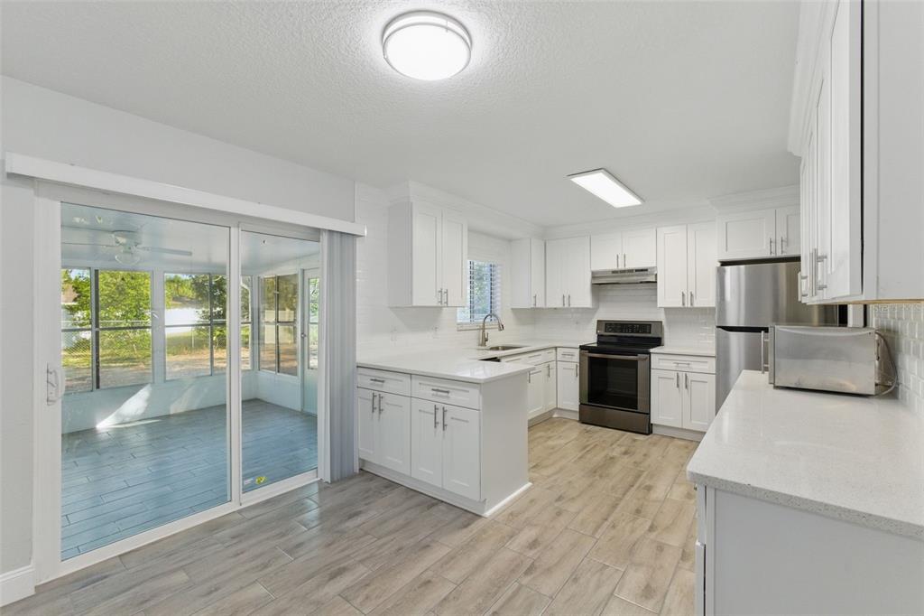 A bright kitchen features white cabinets, stainless steel appliances, and wood-look tile flooring — 8255 PAMLICO STREET, ORLANDO, FL