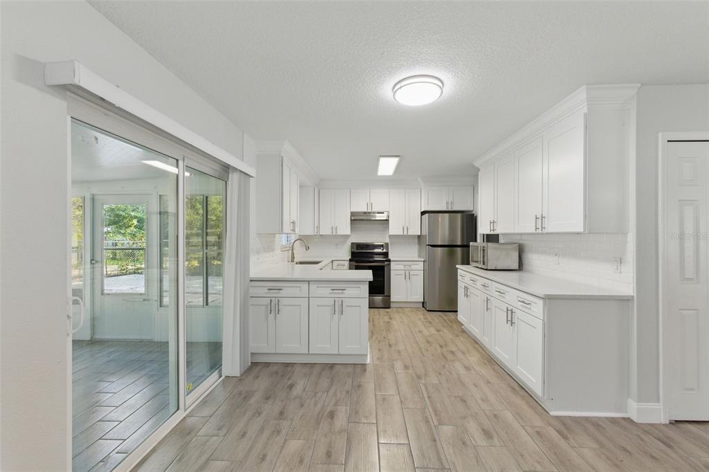 A bright kitchen features white cabinets, stainless steel appliances, and light wood-look flooring — 8255 PAMLICO STREET, ORLANDO, FL