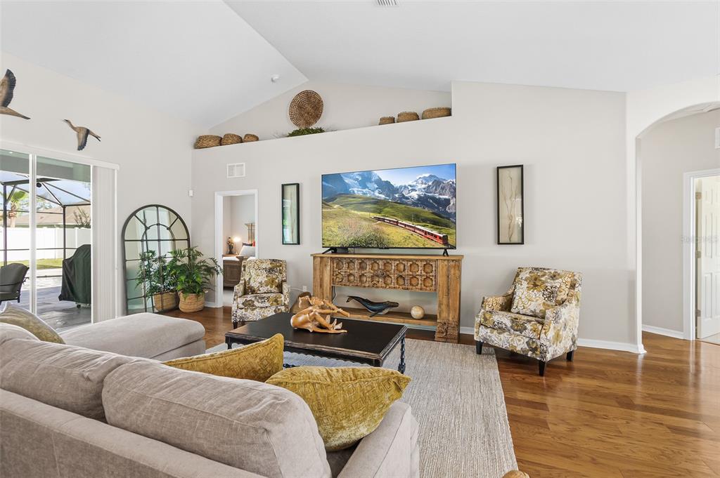 A living room features a vaulted ceiling, hardwood floors, a television, and two patterned armchairs — 116 ERIC DRIVE, PALM COAST, FL