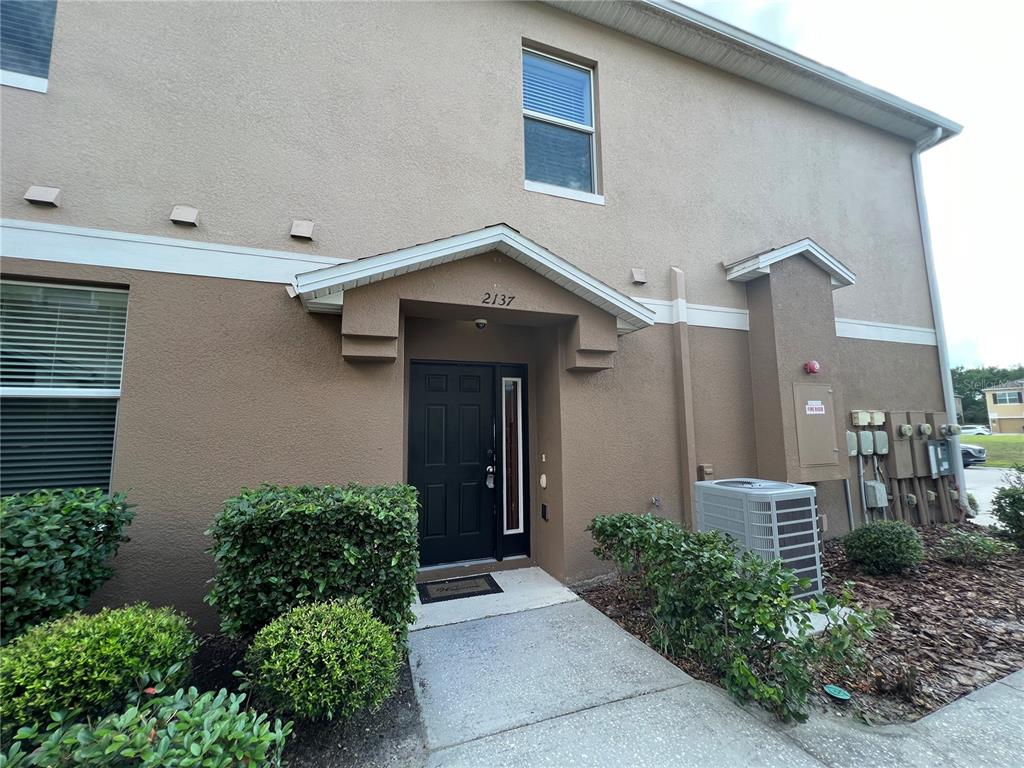A two-story tan stucco building features a black front door under a small gable roof — 2137 BETSY ROSS LANE UNIT 2137, ST CLOUD, FL
