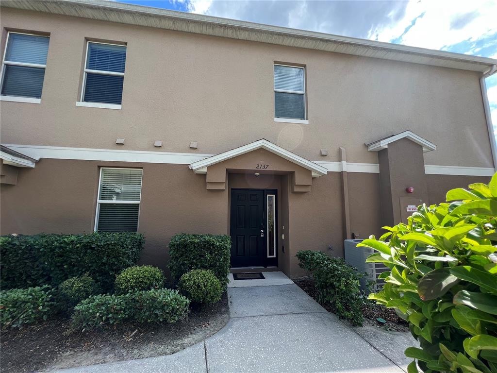 A two-story townhouse exterior features a dark front door, a concrete walkway, and manicured bushes — 2137 BETSY ROSS LANE UNIT 2137, ST CLOUD, FL
