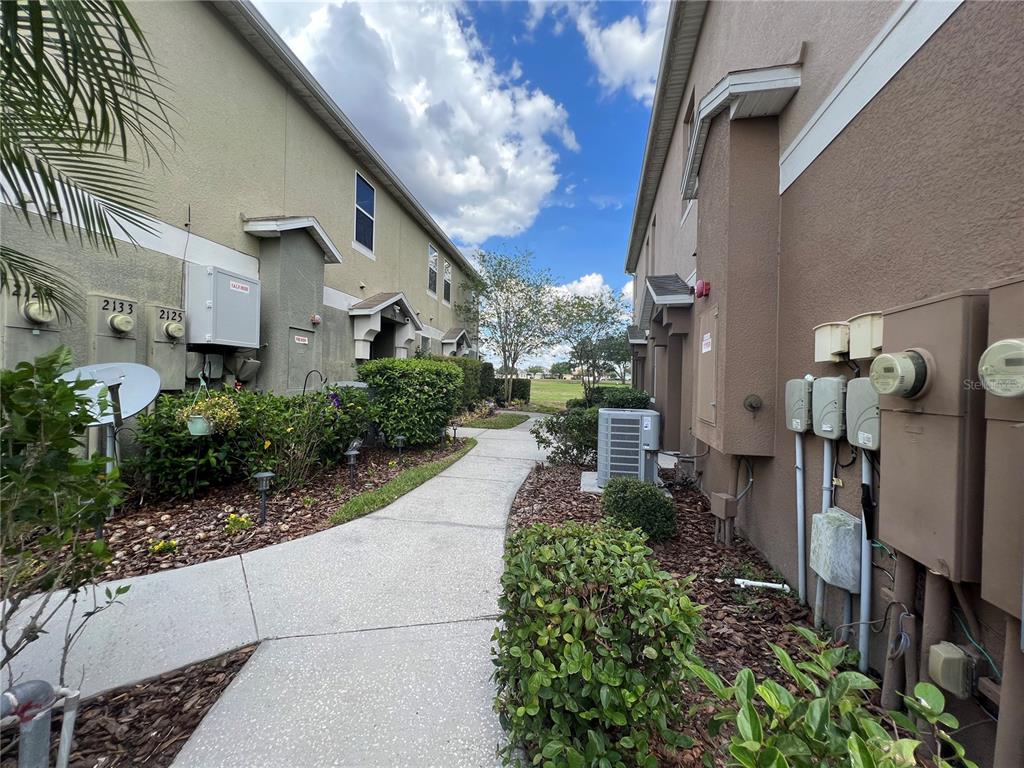 A concrete walkway leads between two multi-story residential buildings with exterior utility meters and landscaping — 2137 BETSY ROSS LANE UNIT 2137, ST CLOUD, FL