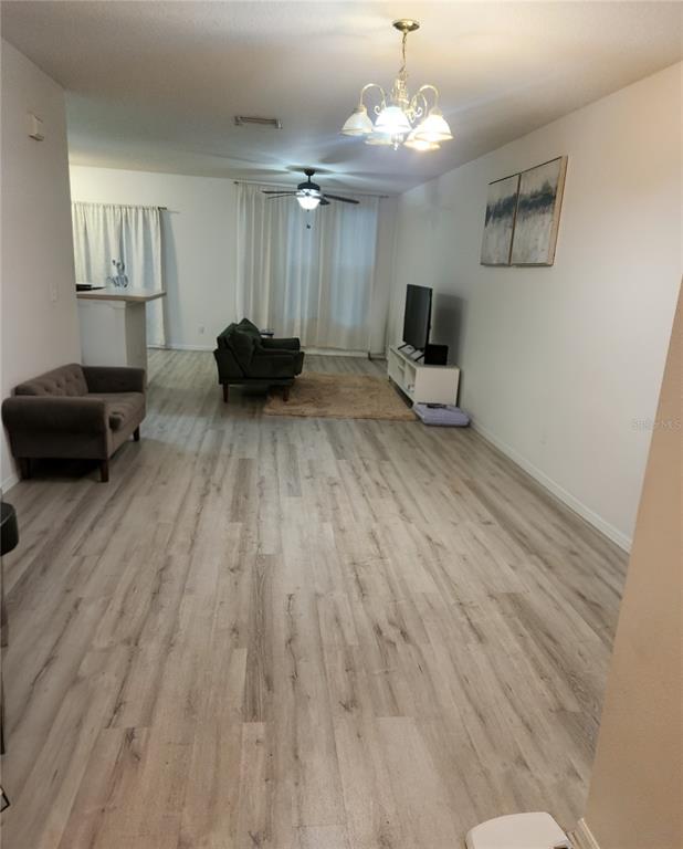 A living room with light wood-look flooring, a ceiling fan, a chandelier, and a television — 9611 CARLSDALE DRIVE, RIVERVIEW, FL