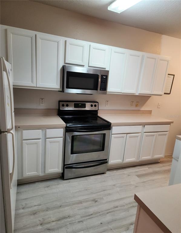 A kitchen features white cabinets, stainless steel appliances, and light-colored wood-look flooring — 9611 CARLSDALE DRIVE, RIVERVIEW, FL