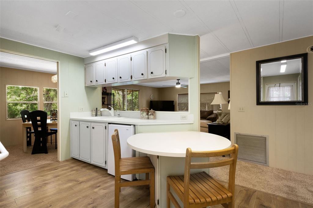 A kitchen features light-colored cabinets, a small dining table, and an opening to the living area — 98 CEDAR ELM DRIVE UNIT 32, SAFETY HARBOR, FL