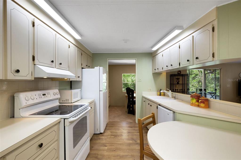 A kitchen features white cabinets, light countertops, wood-look flooring, and a view into another room — 98 CEDAR ELM DRIVE UNIT 32, SAFETY HARBOR, FL