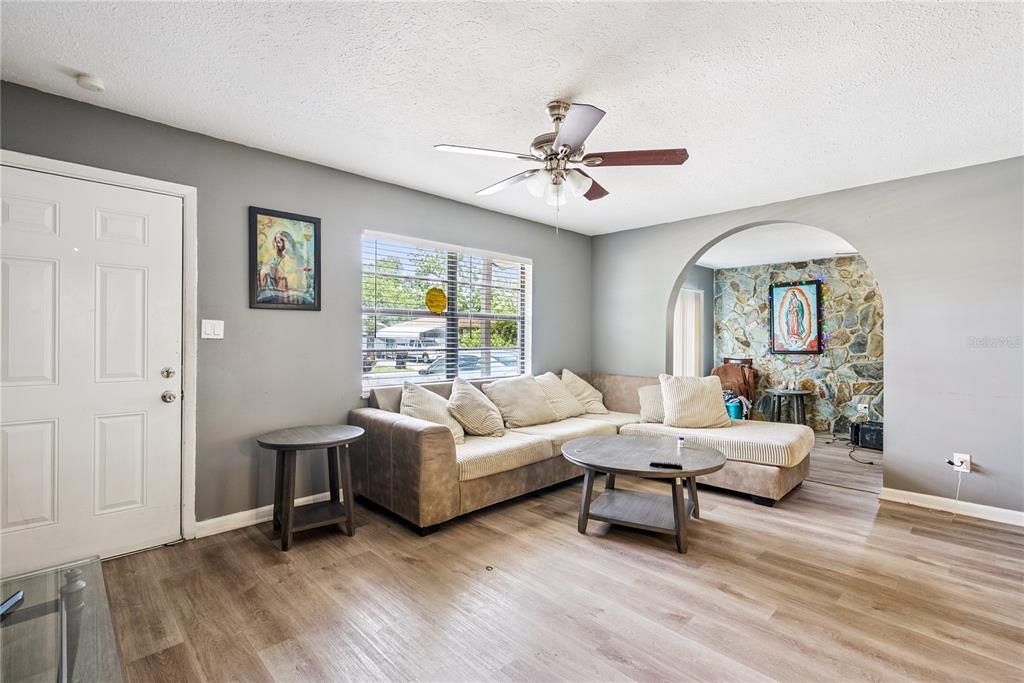A living room features gray walls, wood-look flooring, a sectional sofa, and a stone-accented archway — 1691 LUCY TERRY AVENUE, APOPKA, FL