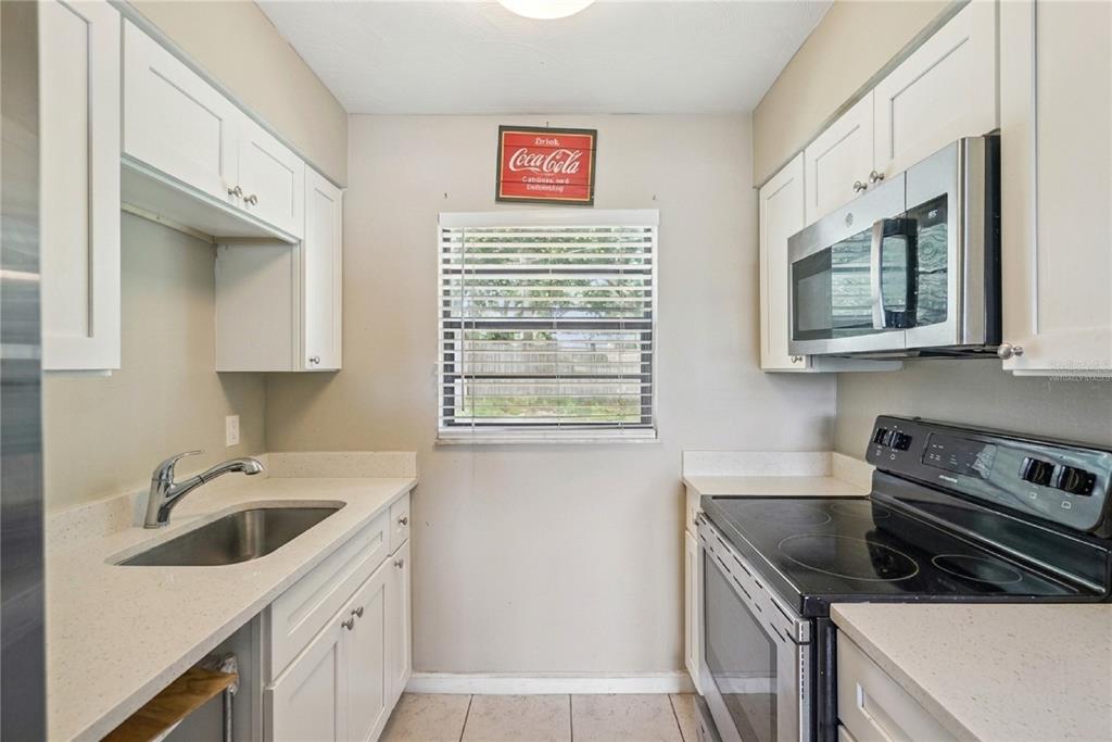 A galley kitchen features white cabinets, light countertops, stainless steel appliances, and a window — 1691 LUCY TERRY AVENUE, APOPKA, FL