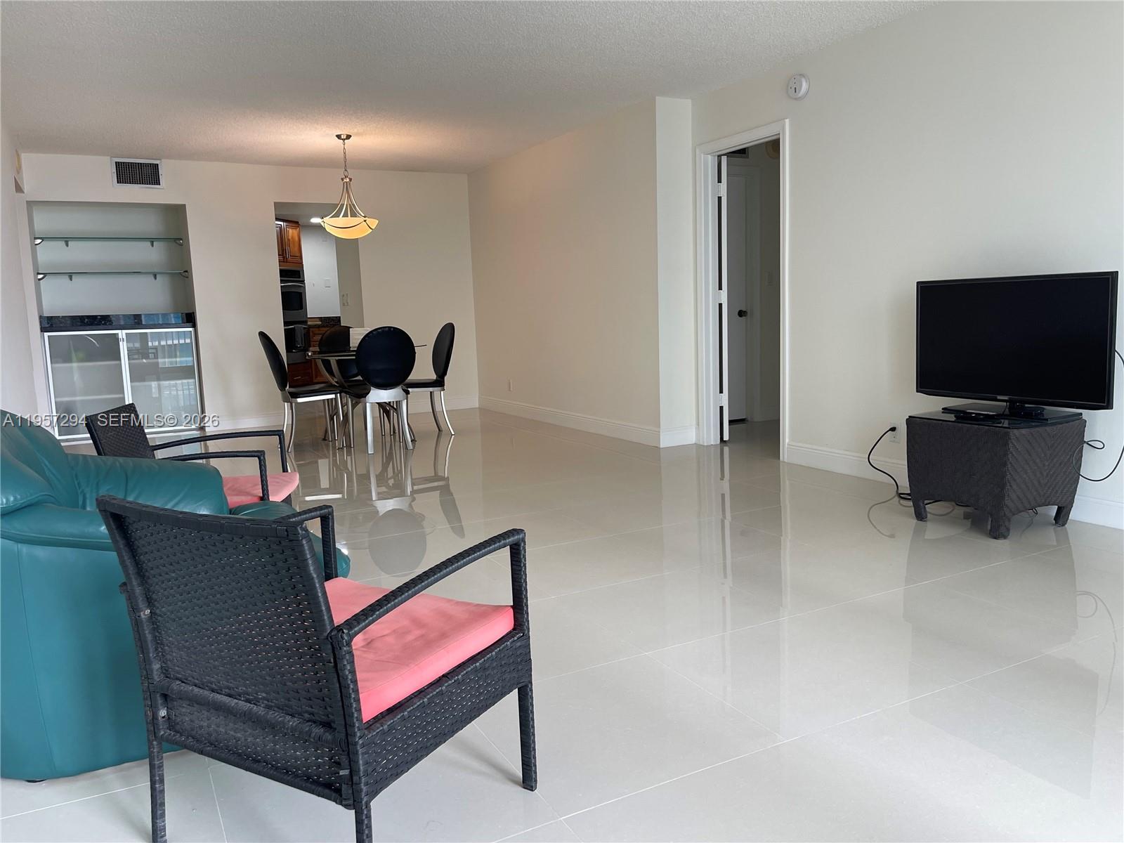 A living room with light tile floors, a television, and a dining area in the background — 1370 S Ocean Blvd # 903, Pompano Beach FL 33062, POMPANO BEACH, FL
