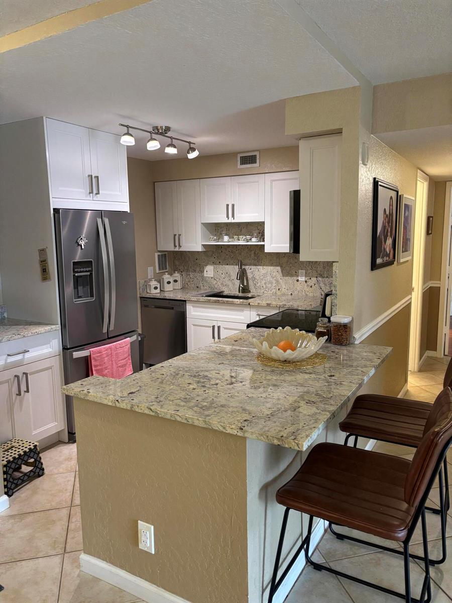 A kitchen features white cabinets, granite countertops, stainless steel appliances, and a breakfast bar — 1000 Spanish River Road # 3c, Boca Raton FL 33432, BOCA RATON, FL